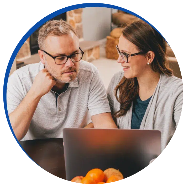 Two homeowners sitting next to each other in front of a laptop at a kitchen table.