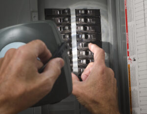 A pair of hands throwing circuit breaker at residential service panel while holding a flashlight up to it.