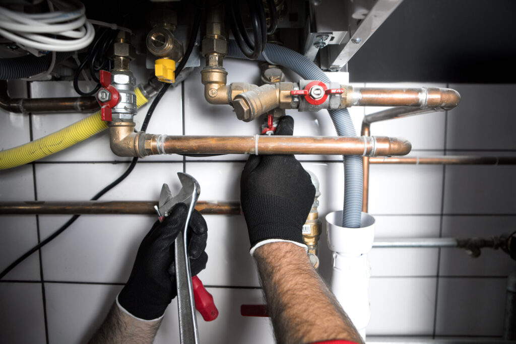 The hands of a plumber wearing black work gloves, working on pipes.